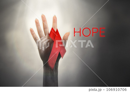 A woman's hand reaches up to light, with a red ribbon on her finger. Dark background with light at the top. The concept of the world day of fight against AIDS and the hope for a cure 106910706
