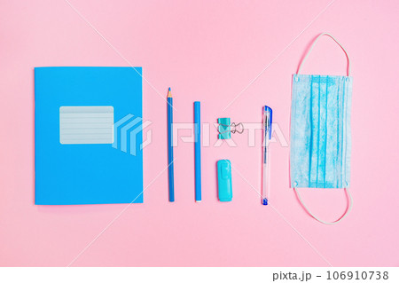 Blue copybook, protective mask and office supplies on pink background. Flat lay. Back to school banner. New normals of education Blue copybook, protective mask and office supplies on pink background. Flat lay. Back to school banner. New normals of education 106910738