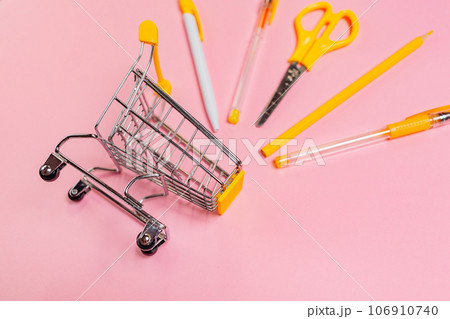 Concept of back to school and shopping. Toy shopping cart with yellow office supplies on pink background Concept of back to school and shopping. Toy shopping cart with yellow office supplies on pink background 106910740