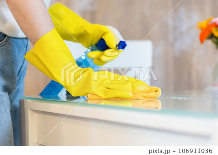 Woman in rubber gloves sprays cleanser and wipes table with rag. Close up. Cleaning service and chores 106911036
