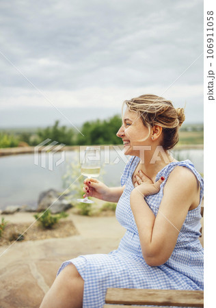 Young attractive woman in a light sundress holds a glass of champagne and laughs. 106911058