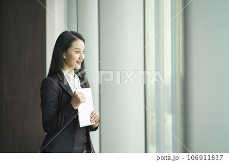 young asian businesswoman standing by window with digital tablet in hand looking out young asian businesswoman standing by window with digital tablet in hand looking out 106911837