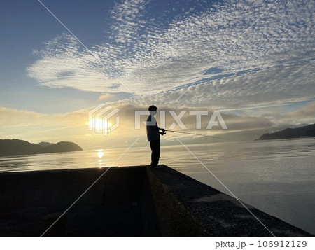 マヅメ時に防波堤で釣りをする青年 106912129