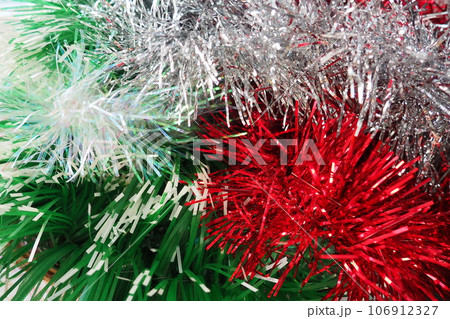 Multi-colored Christmas tinsel. Red, green, silver and white tinsel are intertwined. Festive New Year or Christmas background. Christmas decorations. Decoration of the hall for a party. Christmas boa 106912327