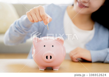 貯金箱にお金を入れる女性 106912624