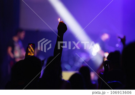 A man in the crowd pulls his hand with a lighter up at a concert 106913606