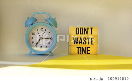 Don't waste time written on wooden blocks on a light background, next to an alarm clock. Don't waste time written on wooden blocks on a light background, next to an alarm clock. 106913619