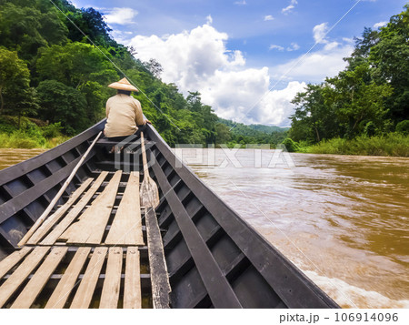 Helmsman with traditional cone hat sails on Pai river with long tail boat, Thailand Helmsman with traditional cone hat sails on Pai river with long tail boat, Thailand 106914096