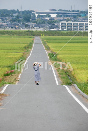 田んぼ道を歩く女性 106914494