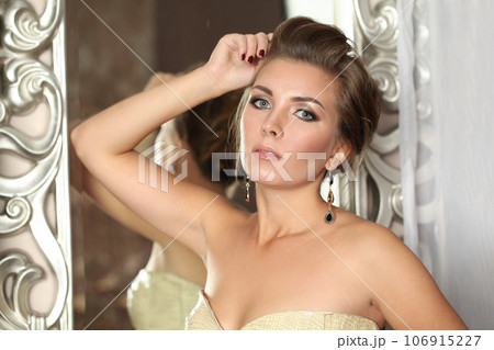 Pretty fashion model woman with makeup and long gold earring, indoor portrait 106915227