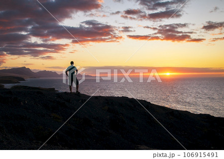 Man looks at the evening over the sea and the bright shining sunset on the Canary Islands in the evening light Man looks at the evening over the sea and the bright shining sunset on the Canary Islands in the evening light 106915491