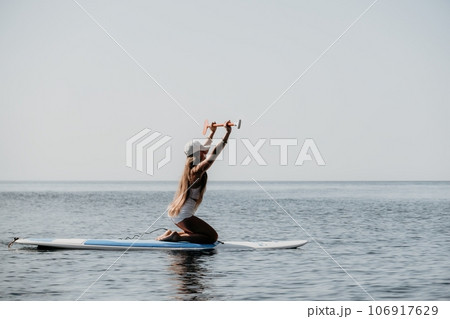 Woman sea sup. Close up portrait of happy young caucasian woman with long hair looking at camera and smiling. Cute woman portrait in bikini posing on sup board in the sea 106917629