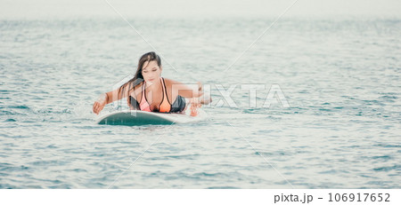 Sea woman sup. Silhouette of happy young woman in pink bikini, surfing on SUP board, confident paddling through water surface. Idyllic sunset. Active lifestyle at sea or river. 106917652