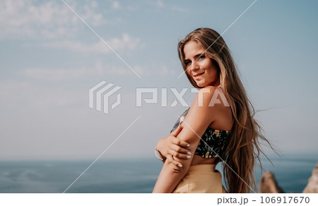 Woman travel sea. Happy tourist taking picture outdoors for memories. Woman traveler looks at the edge of the cliff on the sea bay of mountains, sharing travel adventure journey 106917670