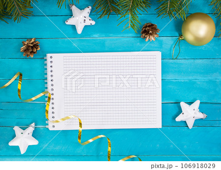 Notepad with white stars, serpentine, pine cones, Christmas ball and spruce branches on blue boards. New Year Notepad with white stars, serpentine, pine cones, Christmas ball and spruce branches on blue boards. New Year 106918029
