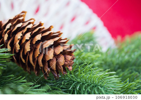 Brown fir cone on spruce branches behind red background with white threads. Christmas, New Year. Copy space Brown fir cone on spruce branches behind red background with white threads. Christmas, New Year. Copy space 106918030