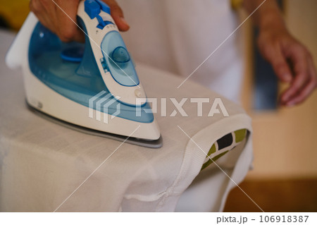 wuman ironing white clothes on the ironing board. Ironing process. Housewife ironing clothes wuman ironing white clothes on the ironing board. Ironing process. Housewife ironing clothes 106918387