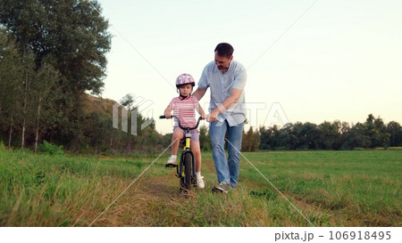 Careful father teaches little girl to ride bicycle in wild summer park 106918495