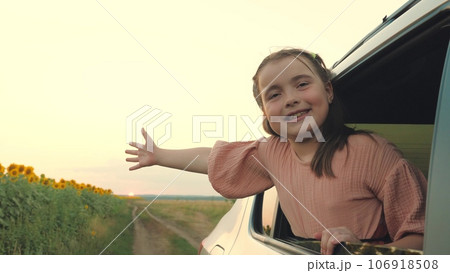 Smiling little girl pulls hand out of car window travelling across farmland 106918508