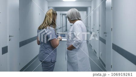 Nurse shows MRI scan image to female doctor in clinic corridor using tablet 106919261