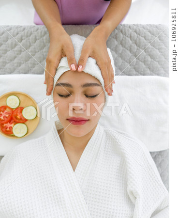 Soak in the tranquil ambiance as a woman luxuriates in therapeutic bliss. Lying on a massage table, her body is expertly attended to by the skilled palms of a masseuse. 106925811