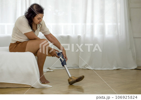 Asian woman disability with prosthetics bionic leg, prosthetic limbs seated calmly on a bed at home. 106925824