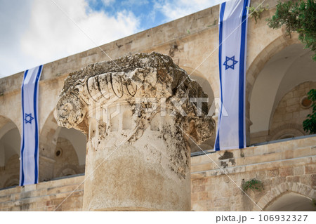 Ancient capital of a column close up with long israeli flags on the background 106932327