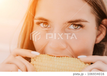 Woman eats corn on beach. Vegetarian hipster woman eat fresh organic grilled corn. Happy lady on sea beach sunset or ocean sunrise. Travel, explore, active yoga and meditation lifestyle concept. 106934016