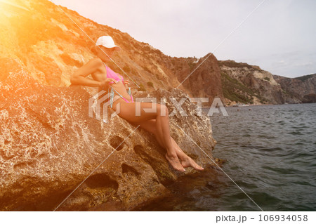 Woman travel sea. Pink bikini tourist captures sea memory, posing on beach amidst volcanic mountains for travel adventure. Happy woman enjoys outdoor photography. 106934058