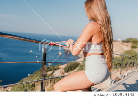 Fitness woman sea. Outdoor workout with fitness rubber bands in park over beach. Female fitness yoga routine concept. Healthy lifestyle. Happy fit woman exercising with rubber band in park. Fitness woman sea. Outdoor workout with fitness rubber bands in park over beach. Female fitness yoga routine concept. Healthy lifestyle. Happy fit woman exercising with rubber band in park. 106934142