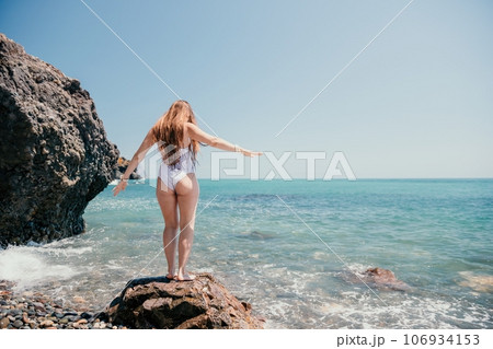Woman sea yoga. Back view of free calm happy satisfied woman with long hair standing on top rock with yoga position against of sky by the sea. Healthy lifestyle outdoors in nature, fitness concept. Woman sea yoga. Back view of free calm happy satisfied woman with long hair standing on top rock with yoga position against of sky by the sea. Healthy lifestyle outdoors in nature, fitness concept. 106934153