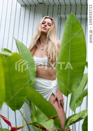 Beautiful young blonde woman in a top with long hair, natural beauty, daylight, in blue glasses, posing against the backdrop of a wooden fence and palm leaves 106938715