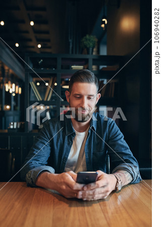 Young bearded businessman,dressed in a denim shirt, sitting at table in cafe and use smartphone. Man using gadget. 106940282