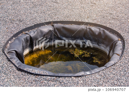 Container for watering plants in the garden. Artificial small pool in the garden for collecting rainwater and watering plants. 106940707