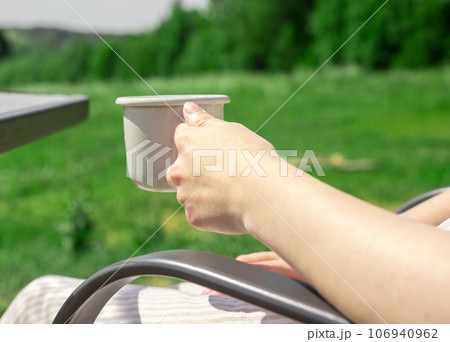 Hand holding tea mug in nature, relaxing outdoors in summer Hand holding tea mug in nature, relaxing outdoors in summer 106940962