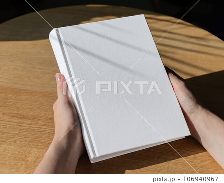 Hands holding book in hard cover mock up on wood table Hands holding book in hard cover mock up on wood table 106940967