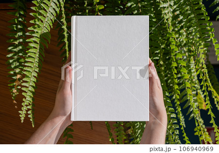 Hands holding book in hard cover mockup among fern leaf Hands holding book in hard cover mockup among fern leaf 106940969