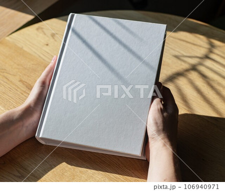 Hands holding closed book mockup on wooden table 106940971