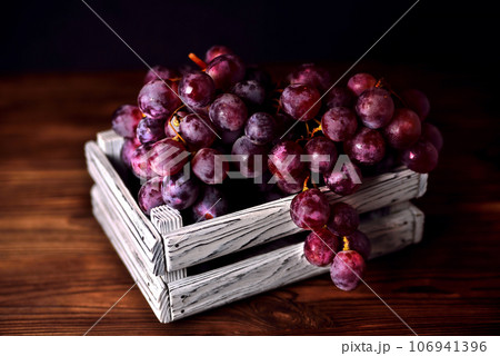 Branch of a dark grapes in a white box on a wooden background Branch of a dark grapes in a white box on a wooden background 106941396