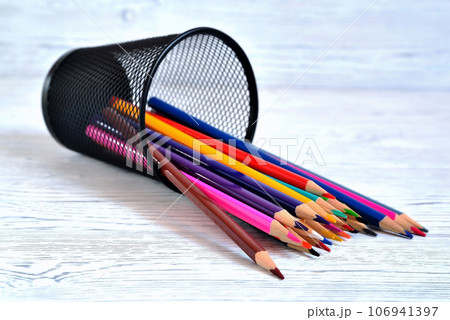 Many multi-colored pencils in a mesh glass on a light natural non-uniform background Many multi-colored pencils in a mesh glass on a light natural non-uniform background 106941397