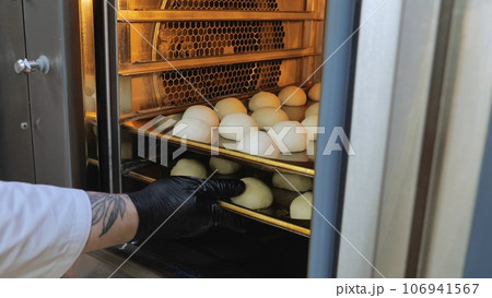 The cook puts the dough in the oven, baking oven, preparation for baking buns, a small oven for baking. The cook puts the dough in the oven, baking oven, preparation for baking buns, a small oven for baking. 106941567