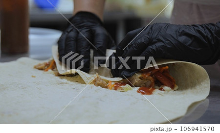 Shawarma in pita bread, shawarma pita vegetables fried potatoes cabbage onions, close-up of the process of cooking shawarma in pita bread, cooking tongs put vegetables on pita bread. 106941570