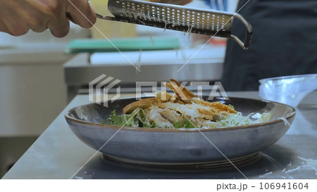 The chef grates cheese on a grater on the finished dish, cheddar cheese is grated, the chef completes the dish, salad with shrimp and grated cheese, close-up 106941604