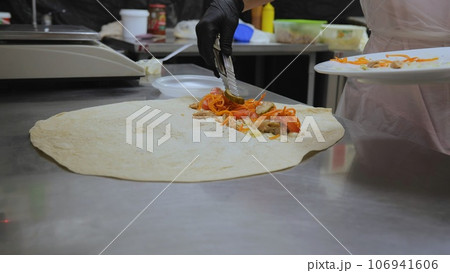 Shawarma in pita bread, shawarma pita vegetables fried potatoes cabbage onions, close-up of the process of cooking shawarma in pita bread, cooking tongs put vegetables on pita bread. 106941606