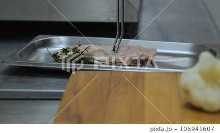 A professional chef prepares a gastronomic dish in a frying pan using ingredients and kitchen utensils. The chef is cooking in the kitchen of the restaurant. Cook's work in the kitchen. 106941607