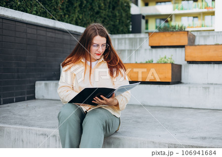 Elegant young 30s woman formally dressed, sitting on the bench and holding a folder with documents. Businesswoman smiling happy standing at the city. Elegant young 30s woman formally dressed, sitting on the bench and holding a folder with documents. Businesswoman smiling happy standing at the city. 106941684