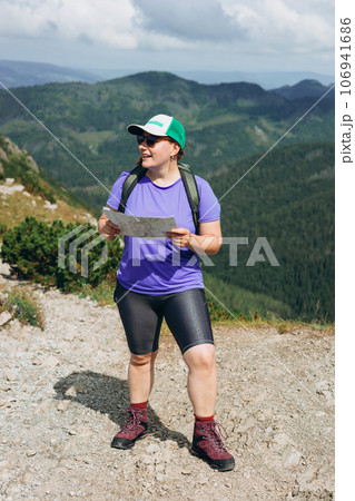 Stylish sport woman holding paper map, wearing backpack and hat looking at mountain view while relaxing in nature. Travel and wanderlust concept. Amazing chill moment. Stylish sport woman holding paper map, wearing backpack and hat looking at mountain view while relaxing in nature. Travel and wanderlust concept. Amazing chill moment. 106941686