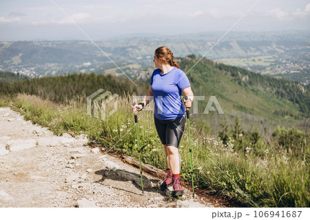 Happy woman hiker with backpack standing on the slope of mountain ridge against mountains. 30s Women holding hiking sticks. Travel and active lifestyle concept, outdoor activities Happy woman hiker with backpack standing on the slope of mountain ridge against mountains. 30s Women holding hiking sticks. Travel and active lifestyle concept, outdoor activities 106941687