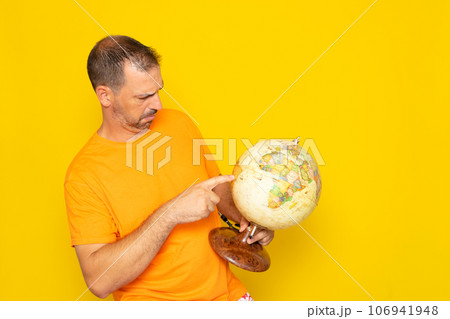 Happy brunette Hispanic man 40 years old, wears orange t-shirt, holds in hands Earth point, world globe, isolated on plain orange background. Stop natural garbage ecology protection concept. 106941948