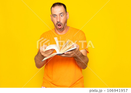 Bearded Hispanic man in his 40s turning the pages of a book visibly excited, isolated on yellow studio background. 106941957